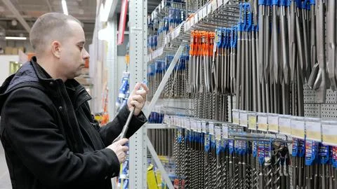 Construction worker comparing drill bit options in hardware store, selecting Stock Photos