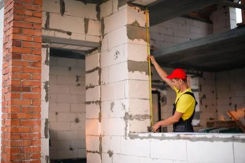 Construction worker at construction site measures the length of window openin Fotos de archivo