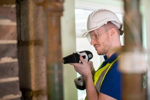 Construction Worker With Cordless Drill Drilling Wall In Renovated House Stock Photos