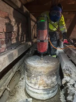 Construction worker core drilling large circular opening in concrete slab. Stockfoto's