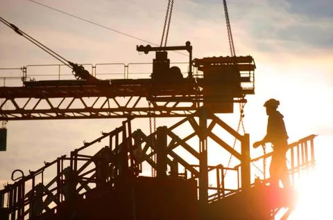Construction worker, crane and building at sunset Stock Photos