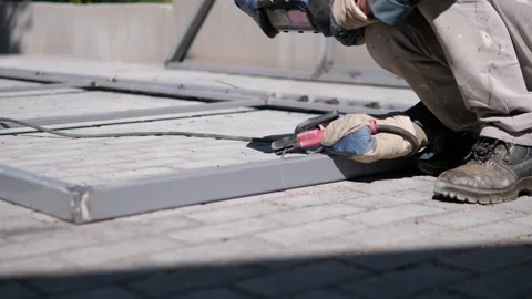 Construction worker crouching on sunlit rooftop using handheld power tool beside Stock Footage 344873521
