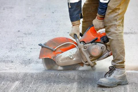 A construction worker cuts old asphalt with a portable petrol saw and a diamo Stock Photos