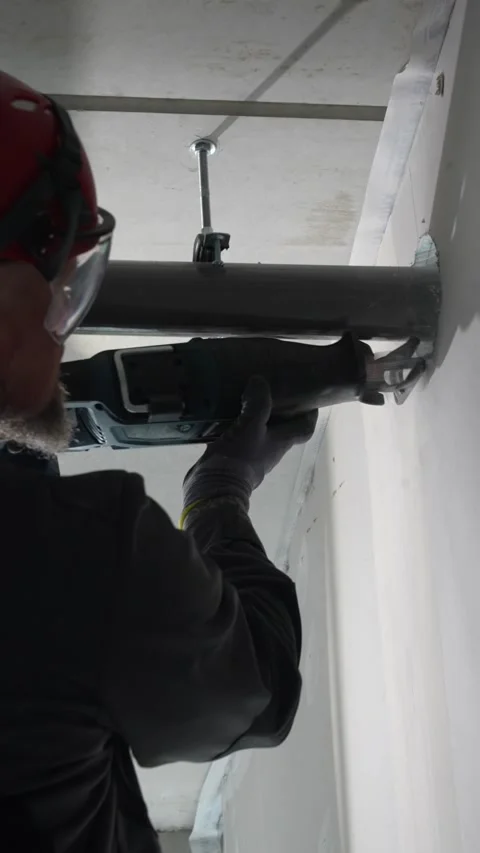 Construction worker cutting mounted metal pipe indoors with reciprocating saw Vidéo 331304632