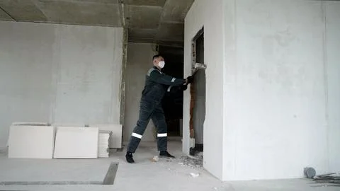 Construction worker demolishing brick wall with sledgehammer inside unfinis.. Stock Photos