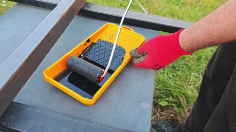 Construction worker dips small paint roller in black bituminous paint, preparing Vidéo 315357884