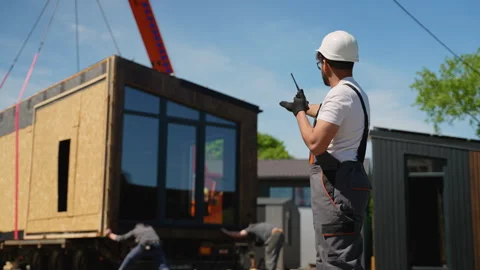 Construction worker directing crane lifting prefabricated tiny house module Stock Footage 316719737