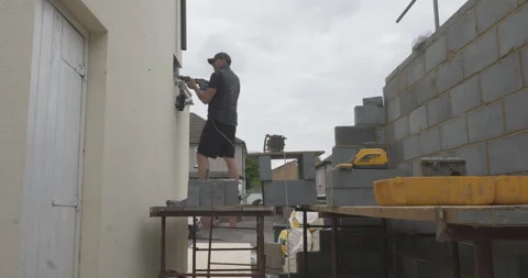 Construction worker drilling a hole into a wall while working on a building site Stock Footage 246379910