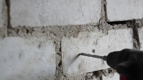 Construction worker drilling a hole into a white brick wall and installing a 動画素材 335277849