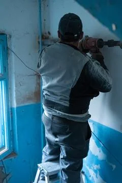 Construction worker drilling into a wall during renovation in an old buildi.. Stock Photos
