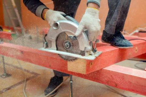 Construction worker with electrical circular saw saws wooden block and a lot of Stock Photos