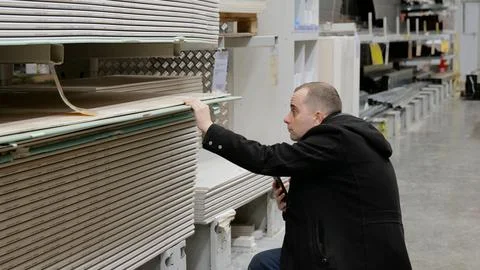 Construction worker examining drywall sheets in hardware store, checking Stock Photos