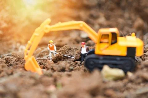 Construction worker figurines working digging ground soil with Backhoe excava Stock Photos