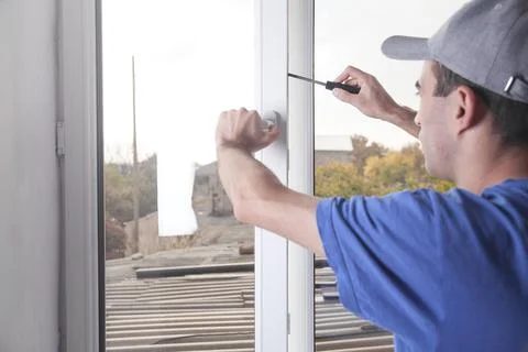 Construction worker fixing window with screwdriver. Installing new plastic wi Stock Photos