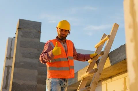 Construction worker gesturing thumbs up on building site with ladder Stock-Fotos