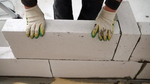 Construction worker in gloves placing a large aerated concrete block while .. Fotos Stock