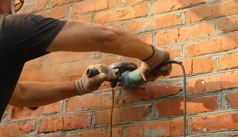 Construction worker with grinder cuts a line in a street brick wall Stock Photos