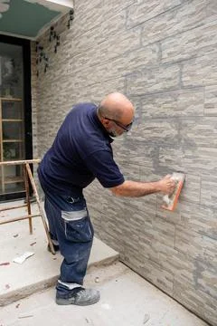 Construction worker grouting stone effect tiles on exterior wall Stock Photos