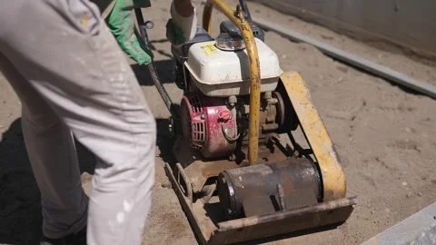 Construction worker guiding compact plate compactor across dusty outdoor Stock Footage 344876242