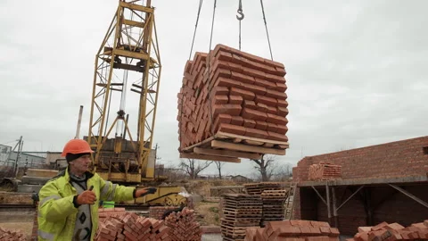 Construction worker guiding crane lifting bricks, A construction worker in a Stock Footage 302749992