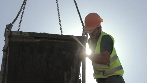 Construction worker handling suspended concrete hopper under strong backlight at Stock Footage 343413624