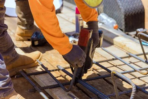 Construction worker hands securing steel bars with wire rods for cement Stock Photos