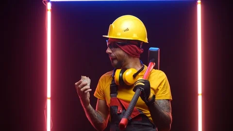 A construction worker in a hard hat with a sledgehammer eats bread Stock Footage 125926198