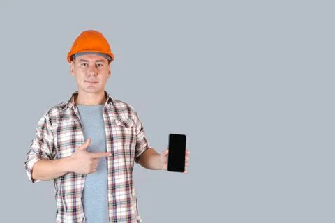 A construction worker in hardhat points to the smartphone screen with his fin Stock Photos
