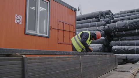 Construction worker in helmet accesses length of profile pipe Stockbeeldmateriaal 255558078