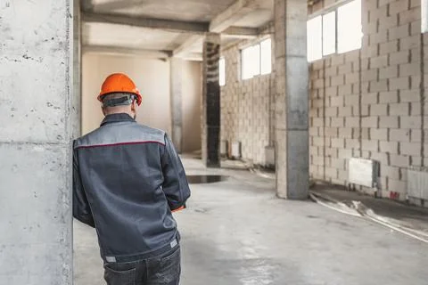 A construction worker in a helmet stands with his back to the camera, leaning on Stock Photos