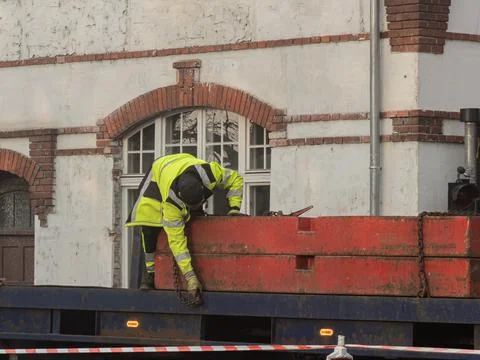 A construction worker in a high visibility jacket secures a heavy red metal Stock Photos