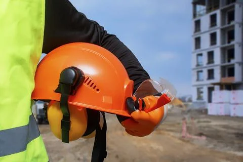 Construction worker in a high-visibility vest holding an orange safety helmet Stock Photos