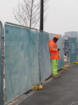 A construction worker in high viz clothes and hardhat looks at his mobile or Stock Photos