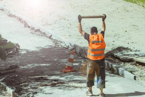 A construction worker hits a pipe on the ground while repairing a road. Stock Photos