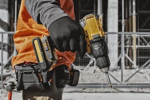 Construction worker holding cordless drill at building site with tool belt an Stock Photos