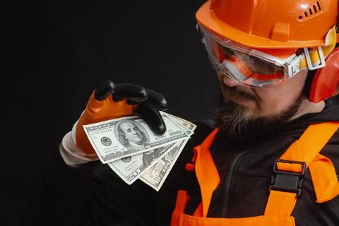 Construction worker holding dollar banknotes in protective gloves. Salary, .. Stock Photos