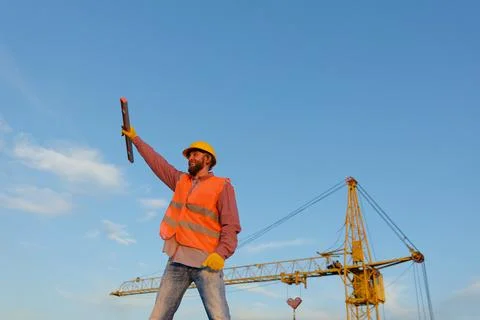 Construction worker holding level tool at building site with crane Stock Photos