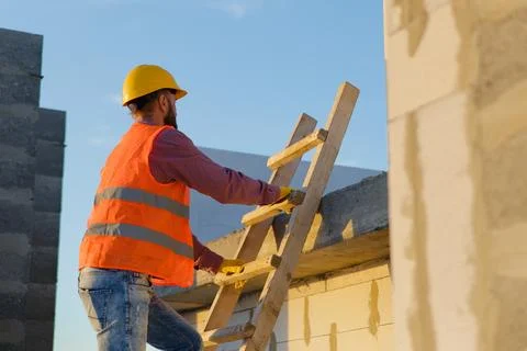 Construction worker inspecting building on ladder at sunset Fotos de archivo