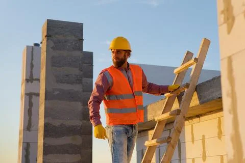 Construction worker inspecting building on ladder at sunset Stock Photos