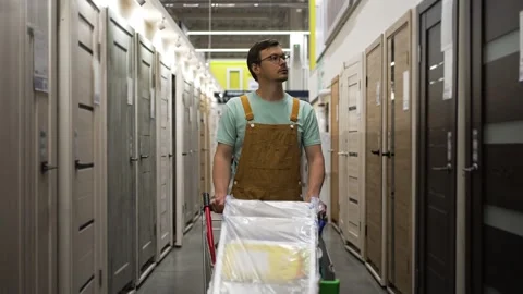 Construction worker inspecting door options at hardware store, selecting Stock Footage 310905549