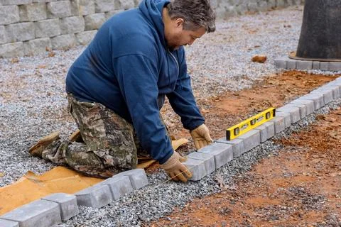 Construction worker installing arranging precast concrete pavers stone for road Stock Photos
