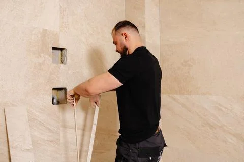 Construction worker installing ceramic tiles on bathroom wall using level too Stock Photos