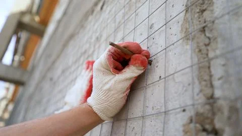 Construction worker installing metal mesh on building wall using nails Stock Photos