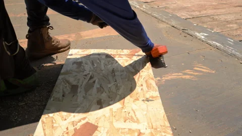 Construction worker installing roofing underlayment on a roof deck using OSB Stock Footage 341547818