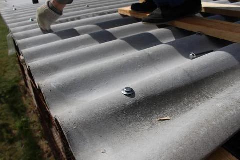 Construction worker installing slate roof covering, hammering metal fastene.. Stock Photos