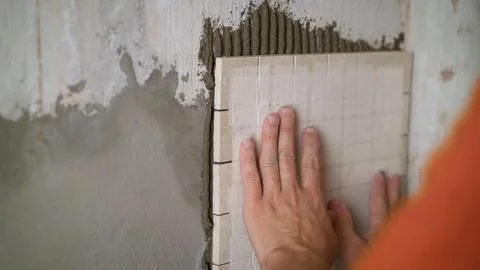 Construction worker installing small ceramic tiles on the wall. Stock Photos