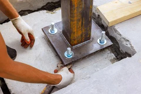 Construction worker installing steel support column on concrete foundation at Stock Photos