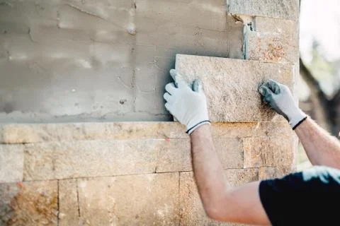 Construction worker installing stone on architectural facade of new building. Stock Photos