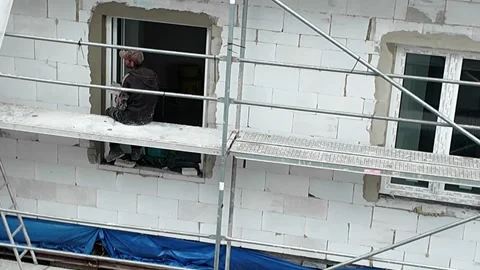 Construction worker installing window frame on scaffolding at new building site. Stock Footage 336757797