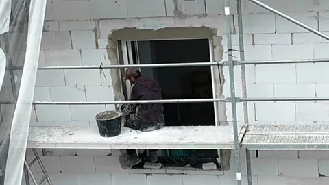 Construction worker installing window frame on scaffolding at building site. Stock Footage 337985464